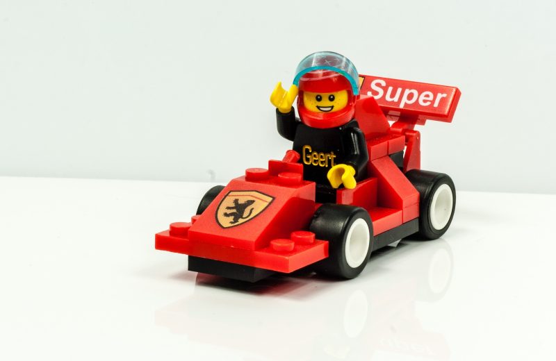 Das Bild zeigt eine gelbe Legofigur in einem roten Rennwagen.