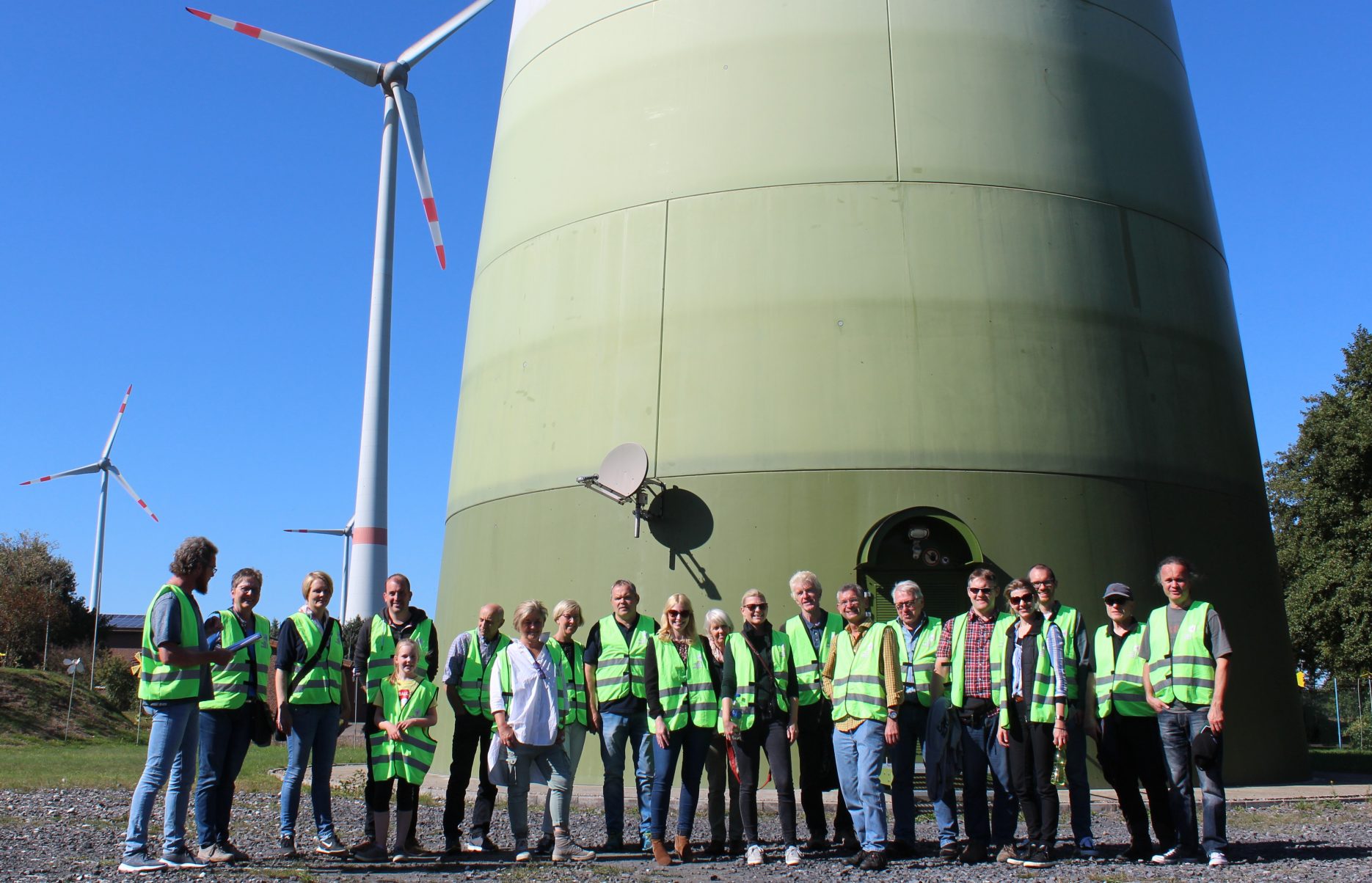 Das Bild zeigt eine Gruppe von Personen in Warnwesten, Teilnehmende des Projektes Klimaschutzbürger 2.0, die am Fuße eines Windrades stehen