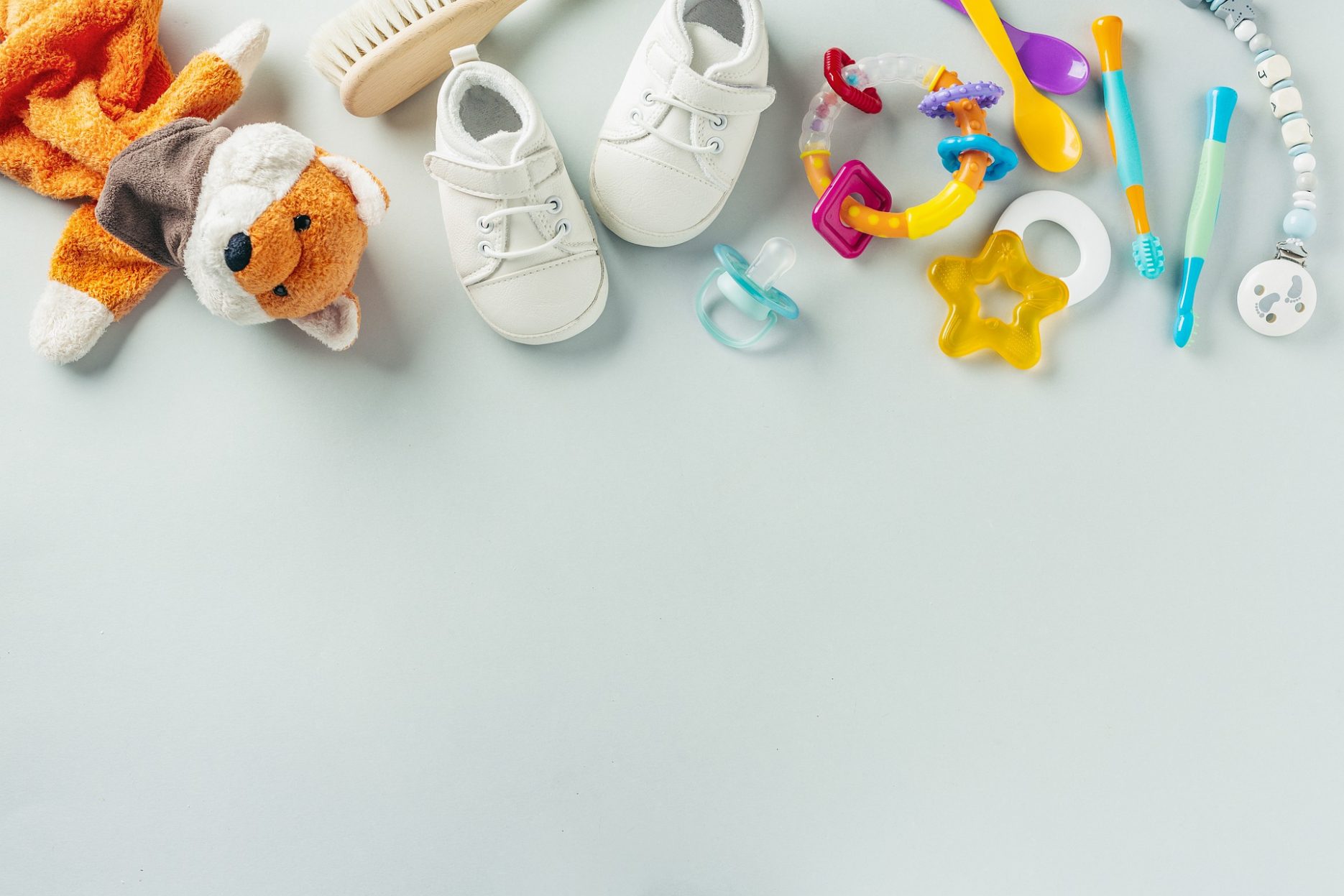 Das Bild zeigt verschiedene, bunte Baby-Sachen: Fuchs-Kuscheltier, Haarbürste, Schuhe, Spielzeug, Schnuller und Schnullerkette, Zahnbürsten, Löffel.