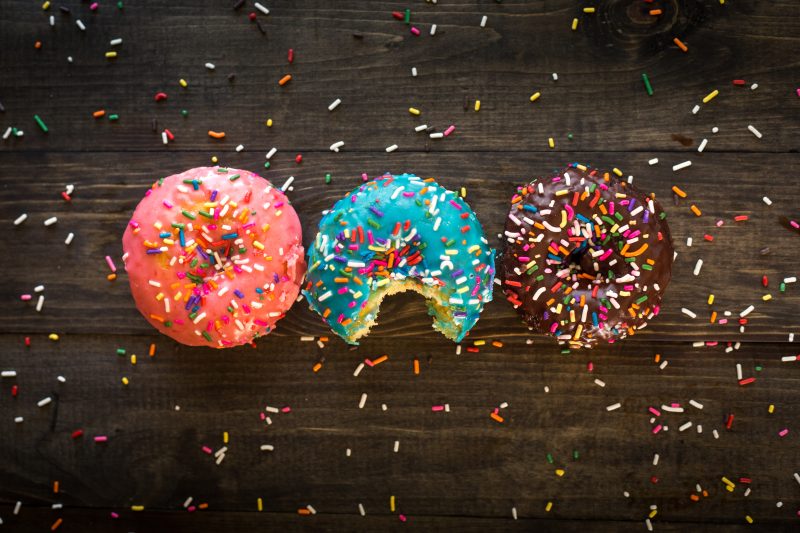 Das Bild zeigt drei Donuts mit buntem Zuckerguss, die nebeneinander liegen.