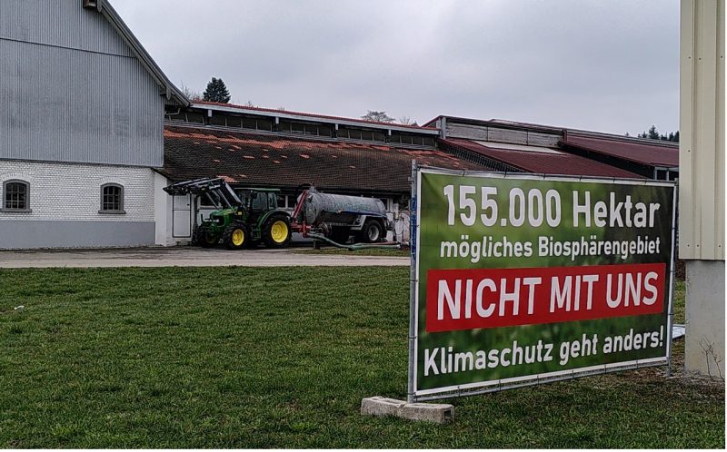 Bild zeigt einen landwirtschaftlichen Betrieb mit einem Traktor und einem Schild auf dem steht: "155.000 Hektar mögliches Biosphärengebiet. NICHT MIT UNS! Klimaschutz geht anders!"